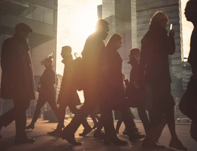 People walking between skyscrapers, silhouetted against the sun.